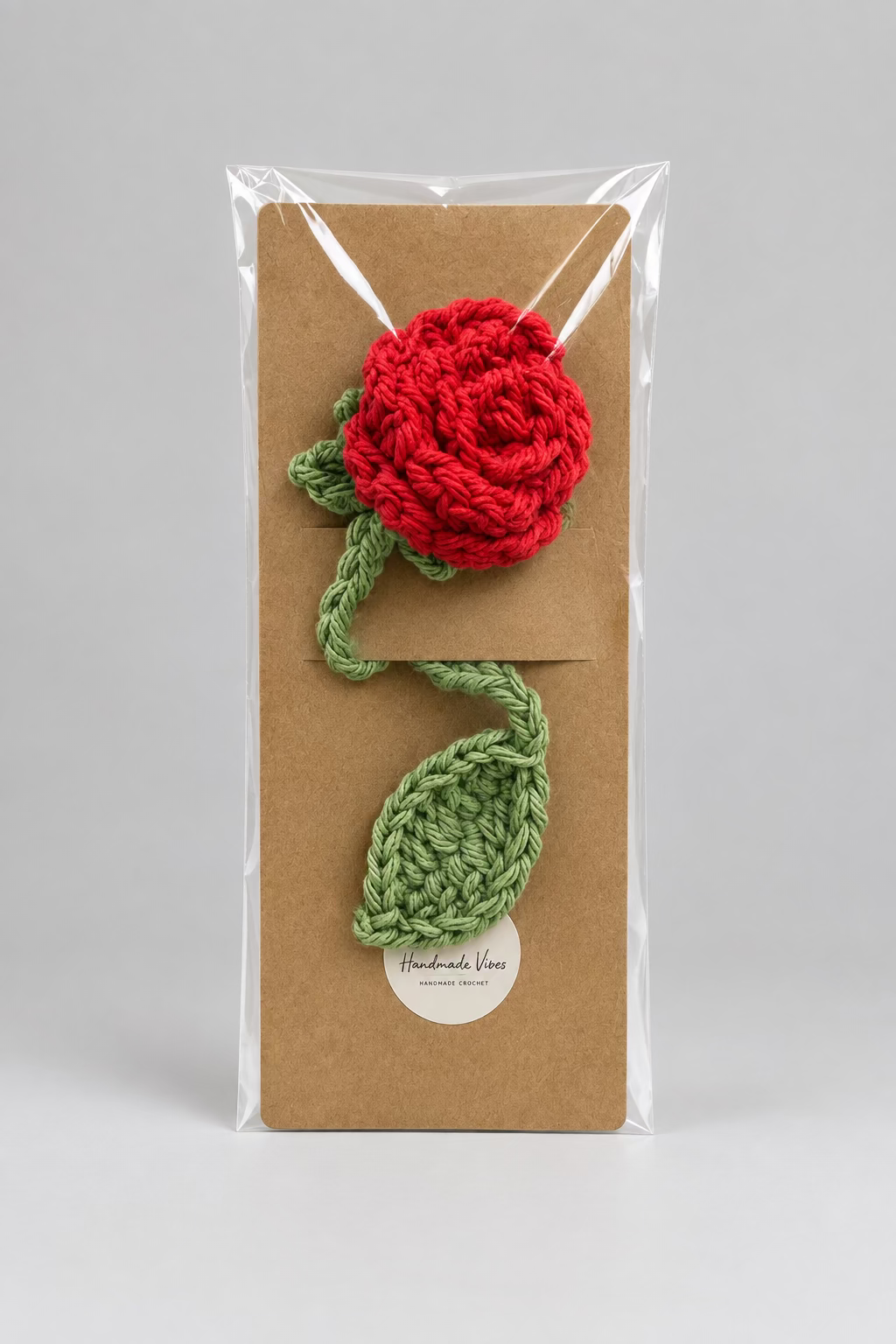 Red and green knitted flower on a brown paper bag with clear plastic wrap.